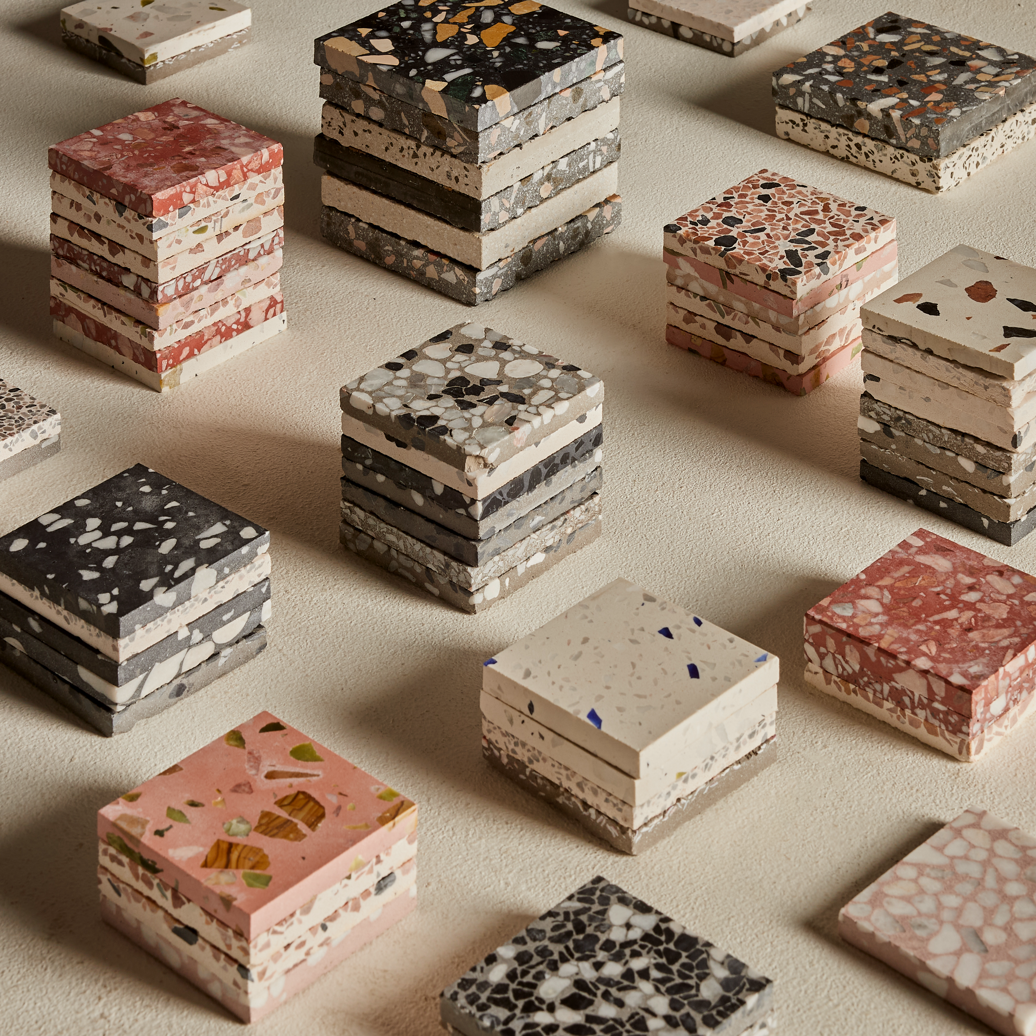 Colorful terrazzo tiles are arranged in stacks on a white plaster surface.